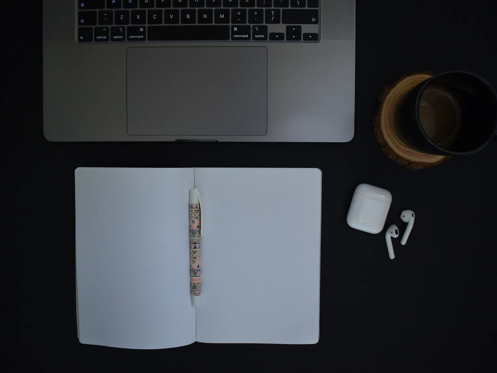 Laptop, aufgeschlagenes Notizbuch und Kaffeetasse auf schwarzem Tisch