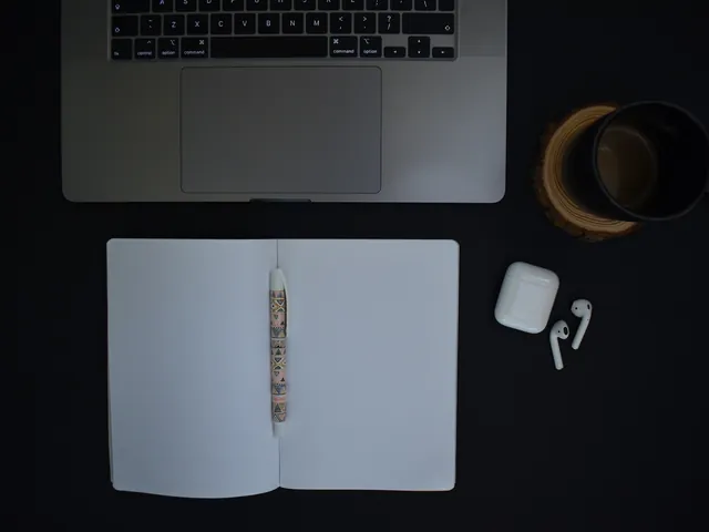 Laptop, aufgeschlagenes Notizbuch und Kaffeetasse auf schwarzem Tisch